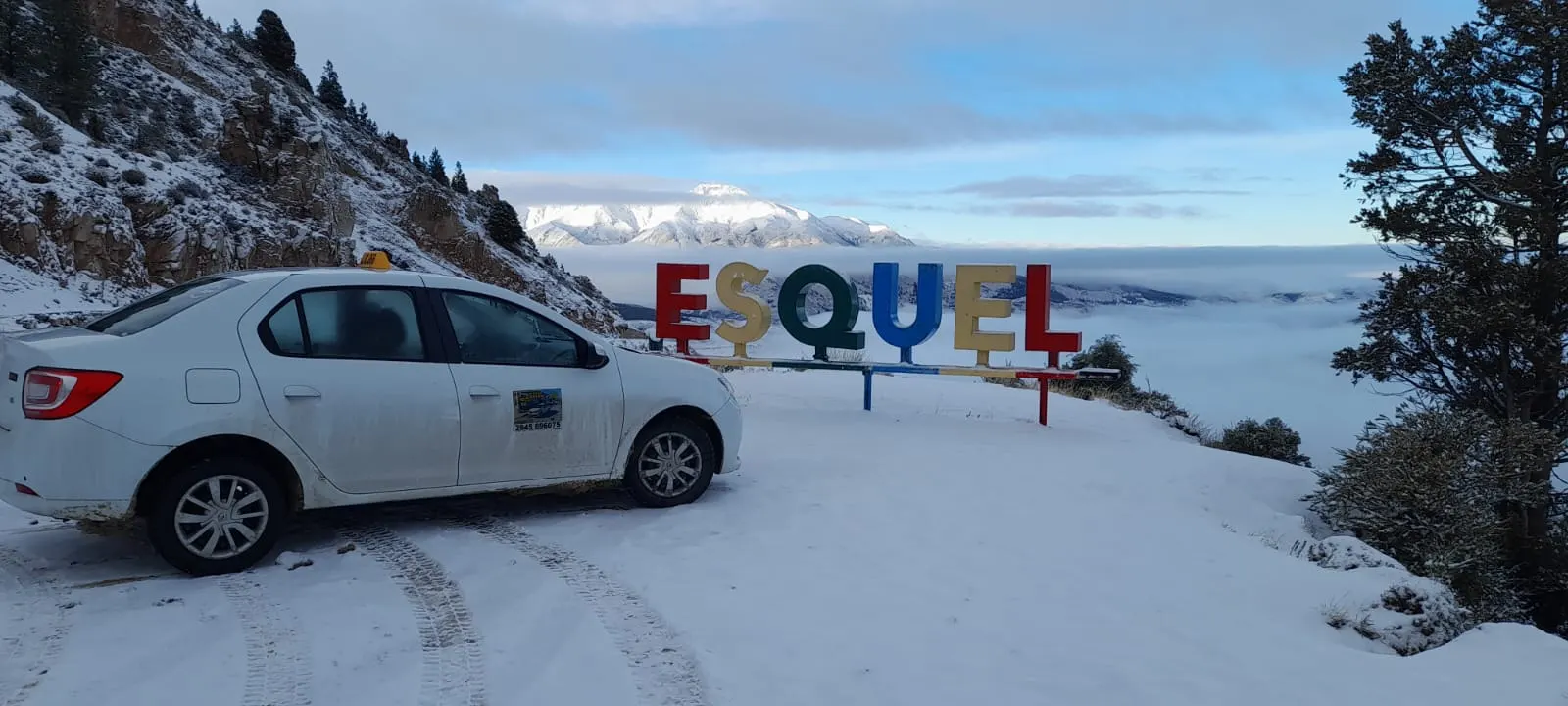 Taxi blanco en un mirador nevado con el cartel de Esquel